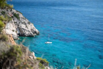 Obraz premium A sailboat rests in turquoise water near a rocky coastline.