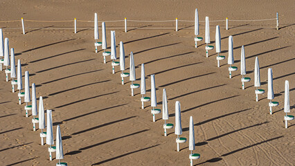 Empty rows of closed beach umbrellas casting long shadows © Luc V. de Zeeuw