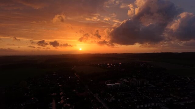 American neighborhood with dramatic clouds against golden sunset in small town. Aerial establishing wide shot. Dark evening scene in spring. Rural countryside hills of USA in distance.