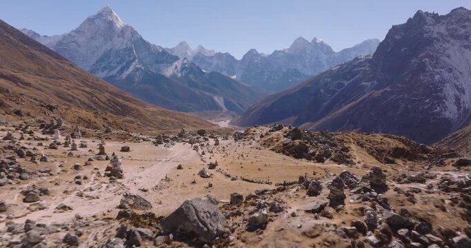 Aerial shot reveal the Everest Memorial Park beside the Everest Base Camp trekking route with dry Himalayan terrain, Khumbu peaks, and Mount Everest rising in the Everest region of Nepal.