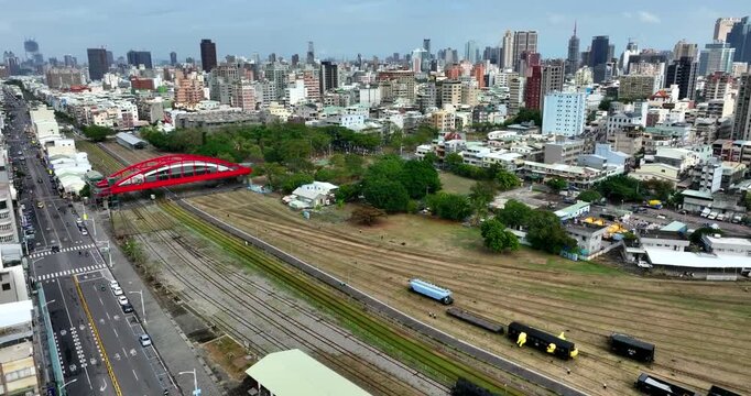 Aerial establishing shot of Kaohsiung city in Taiwan showing green tramway corridor running through dense urban streets with traffic, buildings and modern skyline. Wide shot.