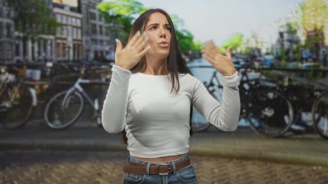 Woman flips hair and raises hands near canal street with parked bicycles and brick buildings; confidence self expression.