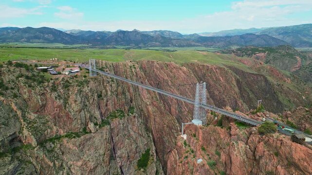 Wide aerial shot of the famous Royal Gorge Bridge spanning across a deep canyon in Colorado, surrounded by rugged mountains and rocky terrain under a blue sky.