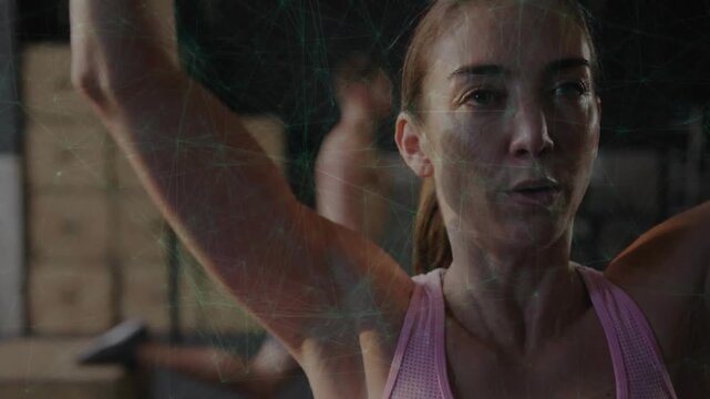 Mid adult woman pressing hex dumbbell from shoulder, facing mirror in gym, building strength
