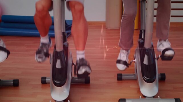 Vertical video: Three riders pedaling bikes in gym, low cut showing ECG line tracking cadence