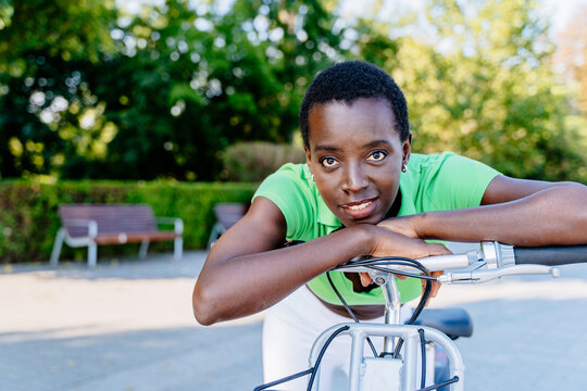 Relaxed ethnic female leaning on city bike in close outdoor portrait