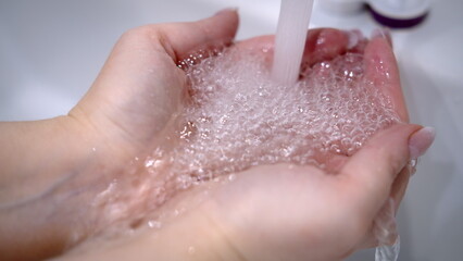 Fototapeta premium water pours through hands at home, water in the bathroom from the tap is pouring through the hands, have fun and enjoy