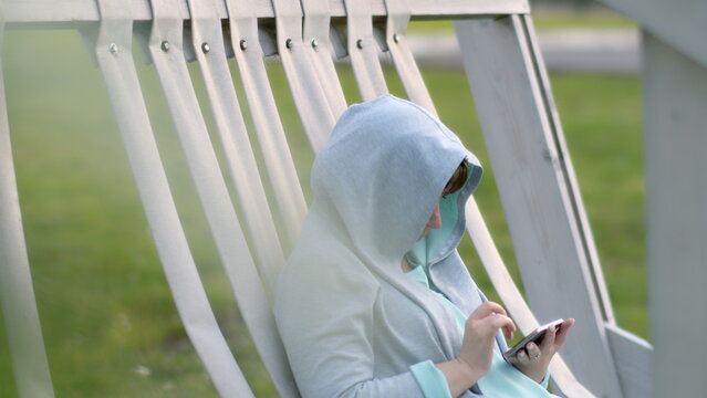 sad woman in the hood uses the phone outdoors in the rest area in the evening, have fun and enjoy