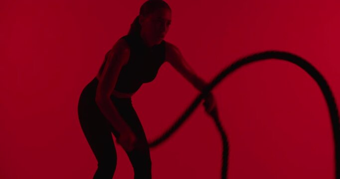 Woman, battle ropes and exercise at gym with fitness, equipment and muscle on red background. Person, strength training and intense challenge with cardio, workout and coordination for wellness