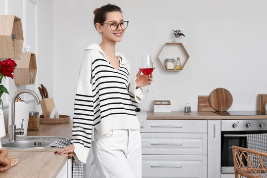 Beautiful young happy woman with glass of red wine in kitchen