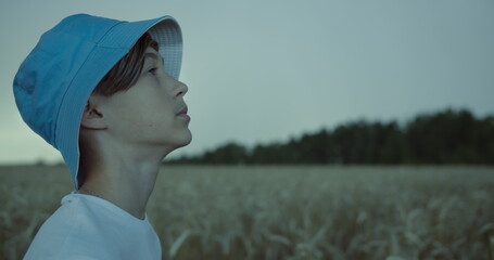 scared boy in a hat stands in a field at the beginning of a storm, boy looks at the sky with horror, strong wind, rain, have fun and enjoy © vla