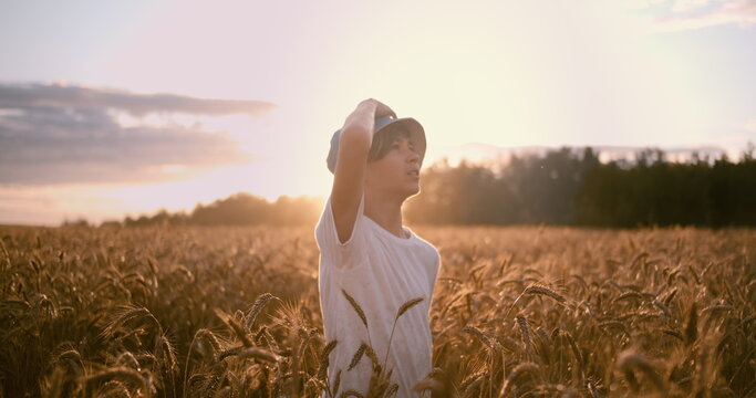 funny boy in a golden wheat field looks at the beautiful sky at sunset before storm, have fun and enjoy