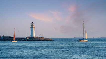 Lighthouse on Pier with Sailing Boats at Sunset