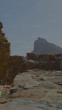 Vertical video: Cam panning, ruins framing sea and mountain, finance graphs rising for insight