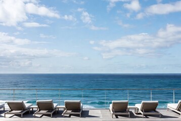 Fototapeta premium Sun loungers on a balcony overlooking the ocean. People are relaxing, enjoying the view. A coastal resort area.