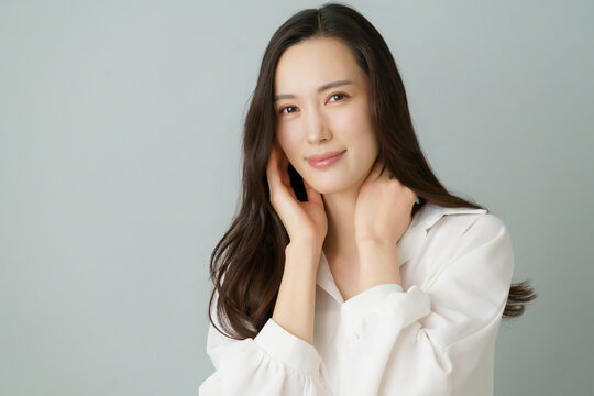 グレーバックの頬に手を当てる白いシャツを着た若い日本人女性のポートレート