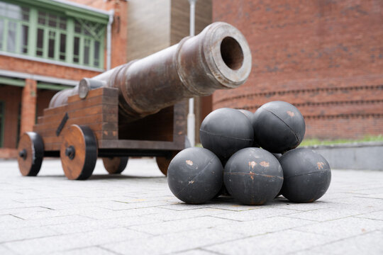 Ancient iron cannon with a stack of cannonballs on a city square.