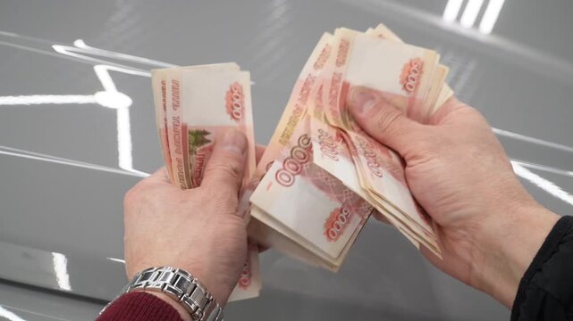 A close-up of a man's hands counts a bundle of bills for five thousand Russian rubles. Man counts red paper 5000 rubles bills. Russian cash money in male hand. A man holds a wad of money in his hands.