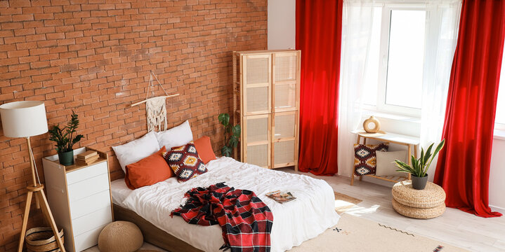 Comfortable bed with soft pillows and wooden folding screen near red curtains in bedroom