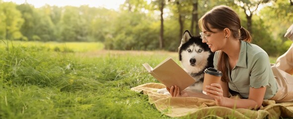 Beautiful woman reading book with cup of coffee and cute Husky dog in park © Pixel-Shot