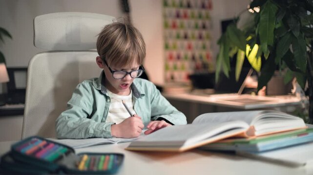 Schoolboy sits at table completely immersed in solving exercises in his notebook
