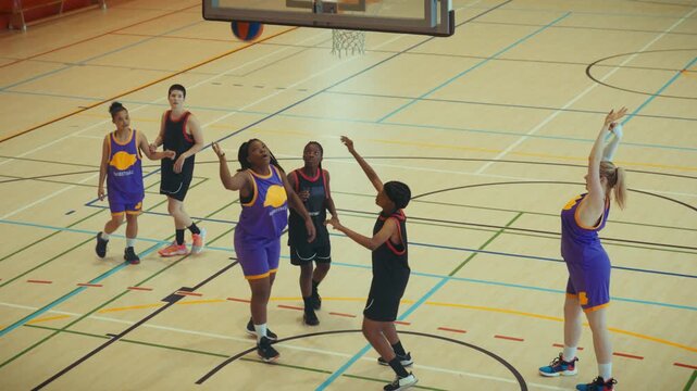A diverse group of young people actively plays basketball on an indoor court. They shoot, pass, and engage in the game, demonstrating teamwork and athletic energy in a dynamic sports setting.