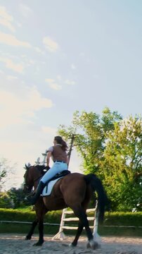 Girl jockey riding a brown thoroughbred stallion jumping a barrier outdoors