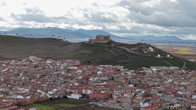 Cinematic drone aerial panning shot of the medieval hilltop castle and iconic white windmills of Consuegra in Castilla-La Mancha, Spain. 