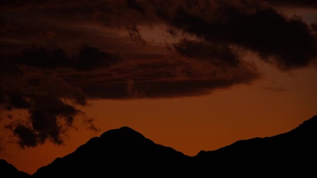 Orange Sunset Sky with Clouds and Mountain Silhouette Timelapse.  Golden Hour Sky with Mountain Silhouette and Clouds Motion. Vibrant Sunset Clouds Above Mountains Time Lapse. 