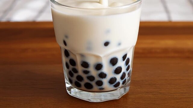 Close up of creamy bubble milk tea with black tapioca pearls in a clear glass on wooden surface