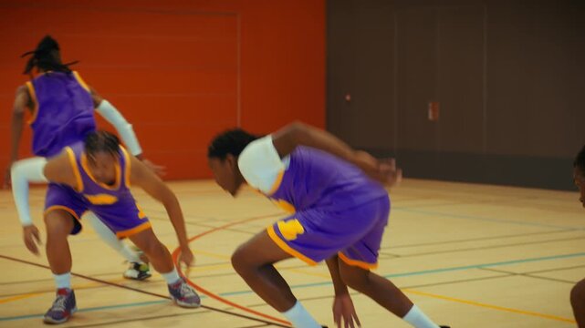 Energetic young men in basketball uniforms perform intense drills on an indoor court. They run sprints and agility exercises, showcasing teamwork, determination, and athleticism in a training session.