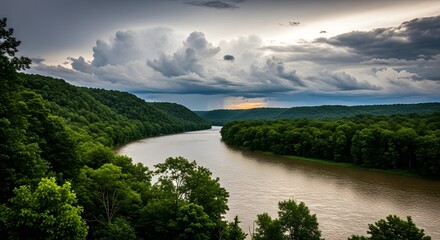 Obraz premium A majestic river carves its way through a lush forested valley under a dramatic cloud filled sky