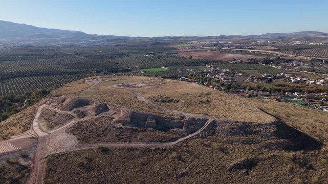 A dramatic upward-moving aerial shot revealing the full scale and structure of the Oppidum &Iacute;bero de Puente Tablas, an ancient Iberian archaeological site nestled in the hills near Ja&eacute;n, Andalusia