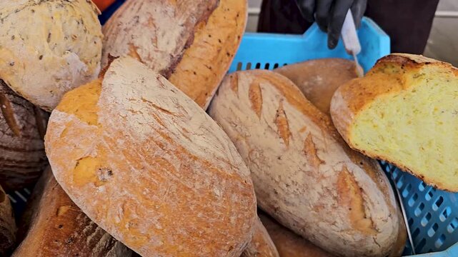 Stacks of rustic homemade bread at outdoor market stall, crusty wheat loaves dusted with flour and scored artisan pattern.