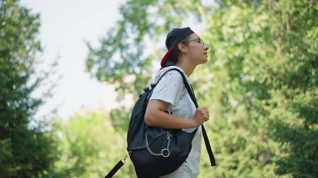 young adult pausing under trees hand in pocket adjusting backpack thoughtful downward gaze reflective mood secluded green clearing soft light portrait study student vibe introspective moment