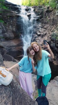 Happy mother and daughter taking a selfie by a forest waterfall in Norway. Authentic family connection, joy, and nature wellness during a summer hike in Northern Europe.