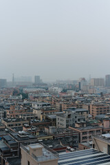 Obraz premium Overhead view of dense urban rooftops in Guangzhou, China under hazy sky with distant skyscrapers