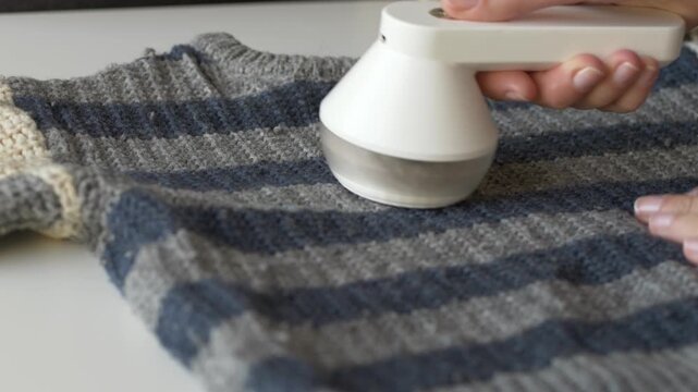 Lint remover cleaning blue wool sweater fabric to extend garment life and reduce clothing waste. Fabric shaver process fits slow fashion, second life textile and responsible consumption visuals.