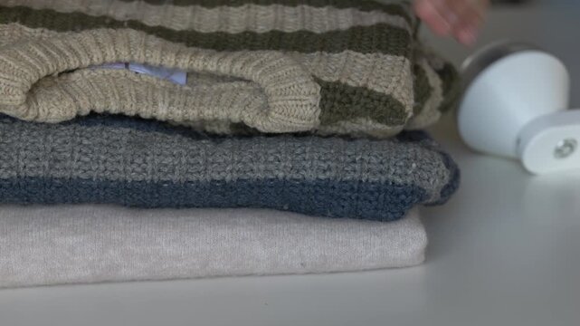 Careful hand handling of old wool sweater being restored for reuse with fabric shaver nearby. Clothing care process fits slow fashion, second life textile and responsible consumption editorial visuals