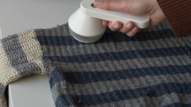 Close-up of lint remover cleaning old sweater fabric to prepare garment for reuse or donation. Fabric shaver process fits slow fashion, second life clothing and responsible textile care visuals.
