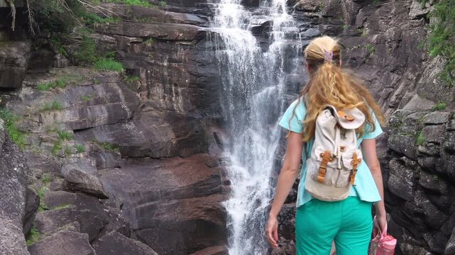 Couple from behind, man and woman embracing and holding hands while looking at a powerful forest waterfall in Norway. Romantic adventure and sustainable travel concept in Northern Europe.