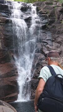 Couple from behind, man and woman embracing and holding hands while looking at a powerful forest waterfall in Norway. Romantic adventure and sustainable travel concept in Northern Europe.