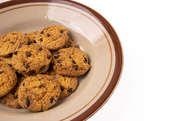 A close-up, partial view of chocolate chip cookies in a ceramic plate, positioned to the left with ample negative space on a white background.