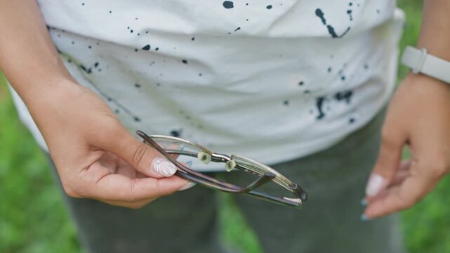 black woman folding patterned sunglasses gently, grasslined park background, neat manicure, careful hinge closure, pocketready accessory, everyday travel habit, calm daily moment