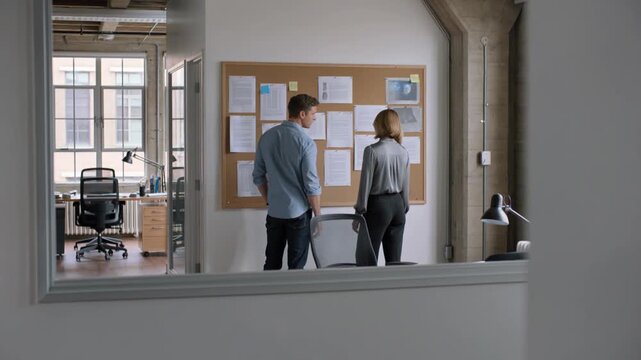 Professional man and woman discussing project details at a corkboard in a modern office, collaborative teamwork and strategic planning for corporate business development