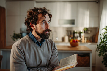 Fototapeta premium Man with curly hair reading, contemplating in kitchen