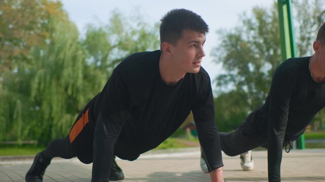 Caucasian men showing focused pushup effort by pond side, closeup facial tension, breath control, strict form and slow descent, steady gaze and determined expression, leafy park backdrop