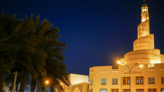 Doha, Qatar - March 19 2025: Abdullah Bin Zaid Al Mahmoud Islamic Cultural Center (Fanar Mosque) illuminated at night with palm trees in Doha.