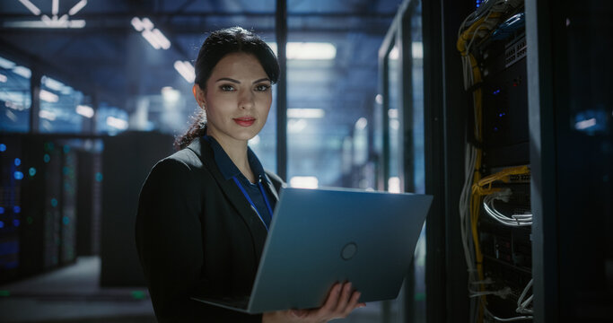 System administrator uses a laptop in data center. Portrait looking in camera. Server racks in server room. Software diagnostics, technical service support for infrastructure 