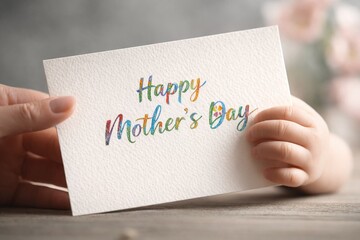 Obraz premium Elegant Happy Mother’s Day card in cursive typography held by a baby's hand and an adult's hand, concept of maternal love, family tenderness, Mother's Day celebration